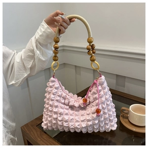 Détail d'un sac à main rose plissé avec poignée perlée et breloques de fermeture ambre