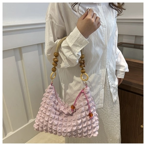 Détail du sac à texture bulles rose avec anse tressée beige et perles en bois