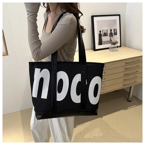 Detail of a large black noco canvas tote bag with leather bottom on a female model shoulder