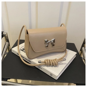 Détail du sac beige avec décoration de nœud argenté et bandoulière à nœuds épais