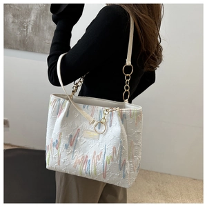 Gros plan sur un cabas blanc avec broderies colorées, chaîne dorée et anse en cuir