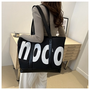 Detail of a large black canvas tote bag with white NOCO letters and long shoulder straps