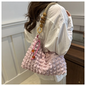 Détail d'un sac à main plissé rose avec bandoulière en perles et tissu bullé