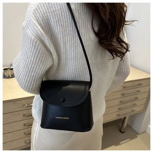 Detail of a black leather crossbody bucket bag featuring gold fashion lettering and flap