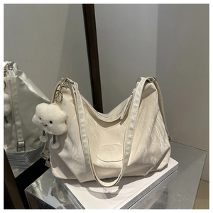 Chic cream hobo bag detail with plush cloud charm and metallic logo on textured surface
