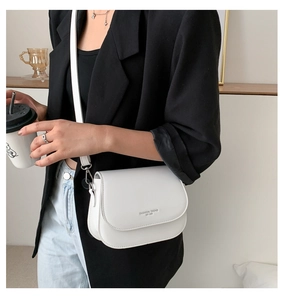 Close-up of white PU leather saddle bag with Fashion Trend EST 1996 text and slim strap