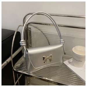 Détail du sac à bandoulière argenté avec nœud sur étagère en verre au décor épuré