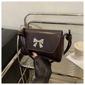 Détail du sac en cuir mat marron foncé avec noeud argenté et bandoulière à nœuds décoratifs