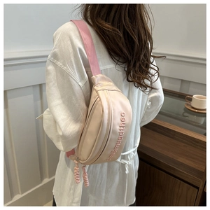Detail view of beige crossbody bag with pink woven strap and embroidered lettering