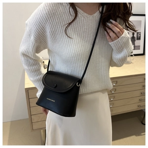 Detail of a minimalist black mini crossbody bag with gold text and button closure