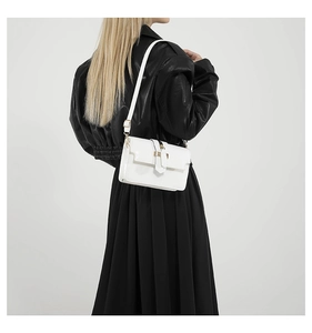 Detail view of a white patent leather square bag with gold buckle and adjustable strap