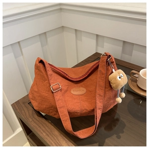 Detail of a burnt orange nylon tote bag with a FASHION patch and plush doll charm