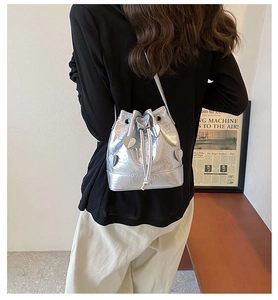 Detail of silver metallic drawstring bucket bag featuring a heart patch and pleated texture