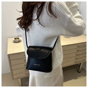 Detail of a minimalist black crossbody bag with gold lettering shown on a model