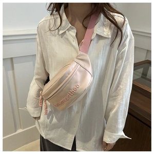 Detail of pink crossbody bag featuring raised relief letters and nylon strap on model