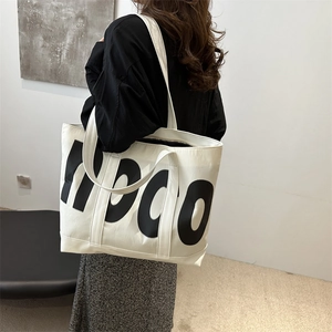 Large capacity white canvas tote bag with black letter pattern shown on a shoulder