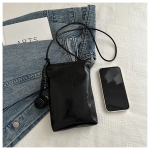 Détail d'un petit sac à bandoulière noir pour téléphone sur un tissu blanc