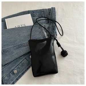 Détail du mini sac de téléphone noir à texture froissée et pendentif boule tressée