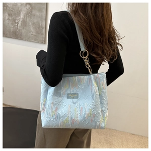 Détail d'un cabas bleu clair avec broderie ondulée et plaque de marque en cuir