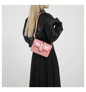Detail of pink patent leather crossbody bag with metal buckle on black leather jacket