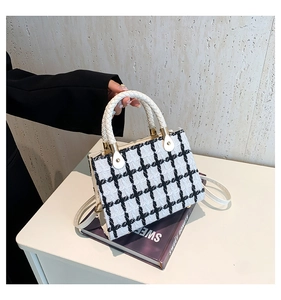 Detail of black and white tweed handbag with woven handles and golden metal accents