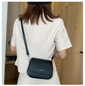 Detail of minimalist black leather saddle bag featuring a fashion trend logo print