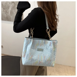 Détail d'un sac cabas en toile bleu clair avec broderie ondulée et chaîne dorée