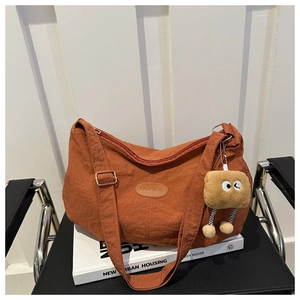 Detail of burnt orange nylon tote bag with fashion tag and plush toy charm on books