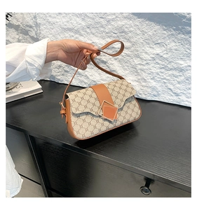 Détail montrant la toile à motif vintage, le rabat en cuir brun et le fermoir doré