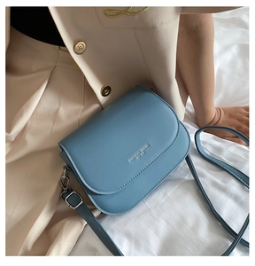 Detail of blue saddle crossbody bag featuring silver fashion trend embossed text