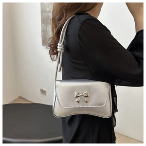 Détail d'un sac à main argenté métallisé avec un nœud en métal chic et une bandoulière fine