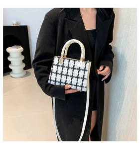 Close-up of black and white tweed handbag with round handles and white strap
