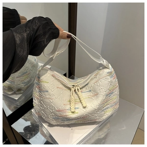 Close-up of white crescent canvas bag with quilted texture and colorful embroidery
