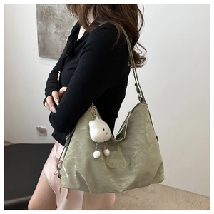 Detail view of large green tote bag with wrinkled texture and plush mascot accessory