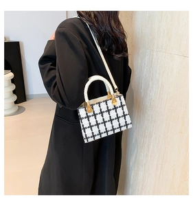 Detail of black and white tweed crossbody bag with woven handle and gold metal hardware