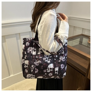 Detailed view of large black tote bag featuring skull and purple floral print on shoulder