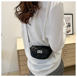 Mini sac bandoulière noir matelassé avec fermoir argenté porté par un mannequin en intérieur