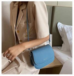Detail of light blue saddle bag with silver lettering on a clean minimalist background