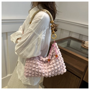 Détail du sac à bandoulière rose gaufré avec sangle en perles de bois sur le modèle