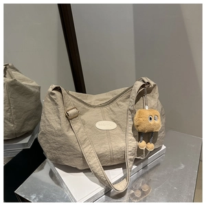 Detail of beige pleated shoulder bag with fashion patch and cute plush doll pendant