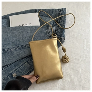 Détail du mini sac carré doré avec bandoulière nouée et texture plissée sur fond denim