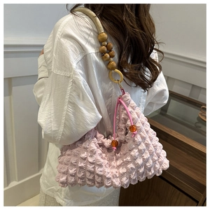 Détail du sac à bandoulière plissé rose avec bandoulière en perles de bois sur modèle