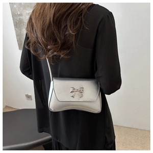 Détail d'un sac à bandoulière argenté métallisé avec un nœud décoratif en métal
