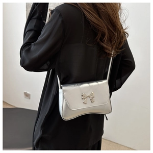 Sac bandoulière argenté avec nœud chic porté sur une tenue sombre pour le quotidien