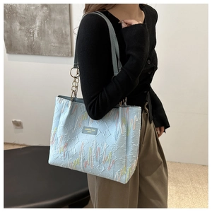 Détail du sac cabas bleu clair avec broderie ondulée et bandoulière en chaîne dorée