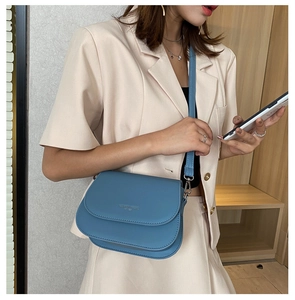 Close-up of blue leather saddle bag with adjustable strap worn with a beige suit