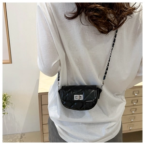 Détail d'un sac bandoulière matelassé noir avec chaîne argentée porté par un modèle