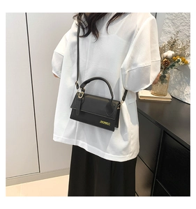Close-up of a minimalist black leather crossbody bag featuring gold letter logo detail
