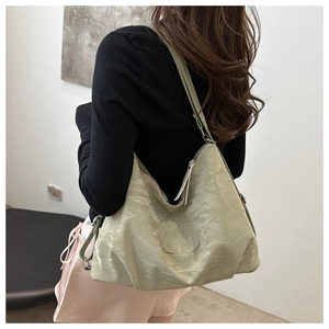 Sage green tote bag with pleated texture shown on shoulder in a minimalist indoor setting