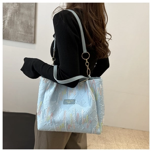 Détail d'un sac cabas bleu clair avec lettres gaufrées et texture brodée colorée